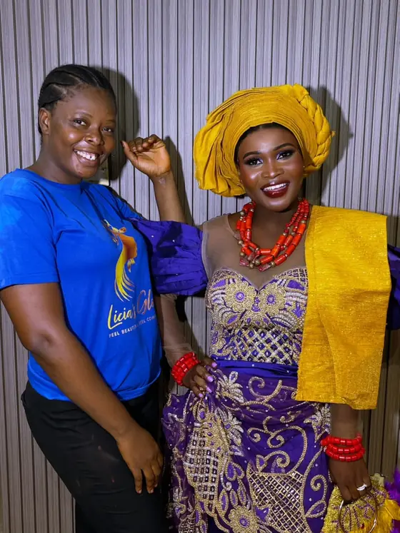 A Licia's Glow student smiling beside the finished makeup and headwrap look she created