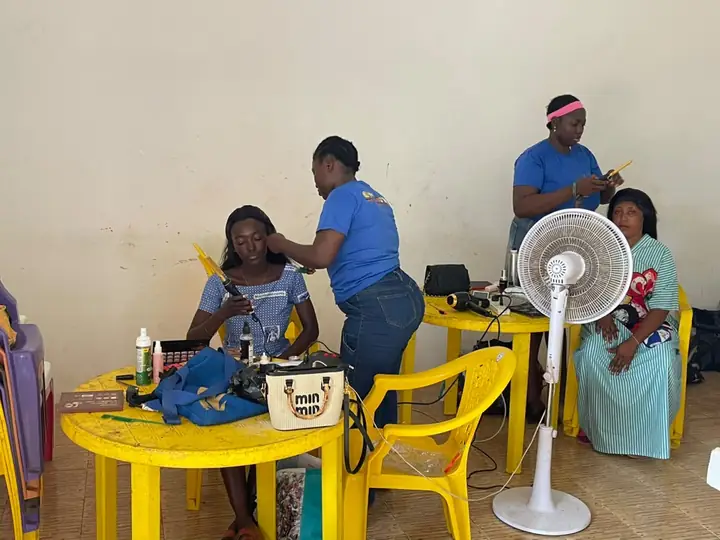 Students doing makeup and hair at yellow tables with a fan and their tools laid out
